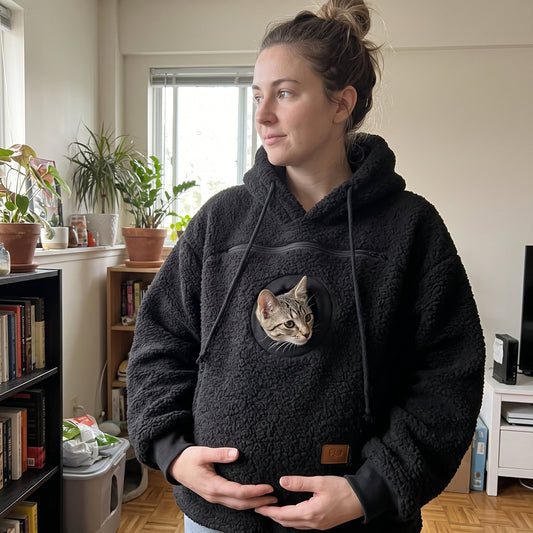 Tabby cat peeking out of the pouch of a black Pawdie hoodie