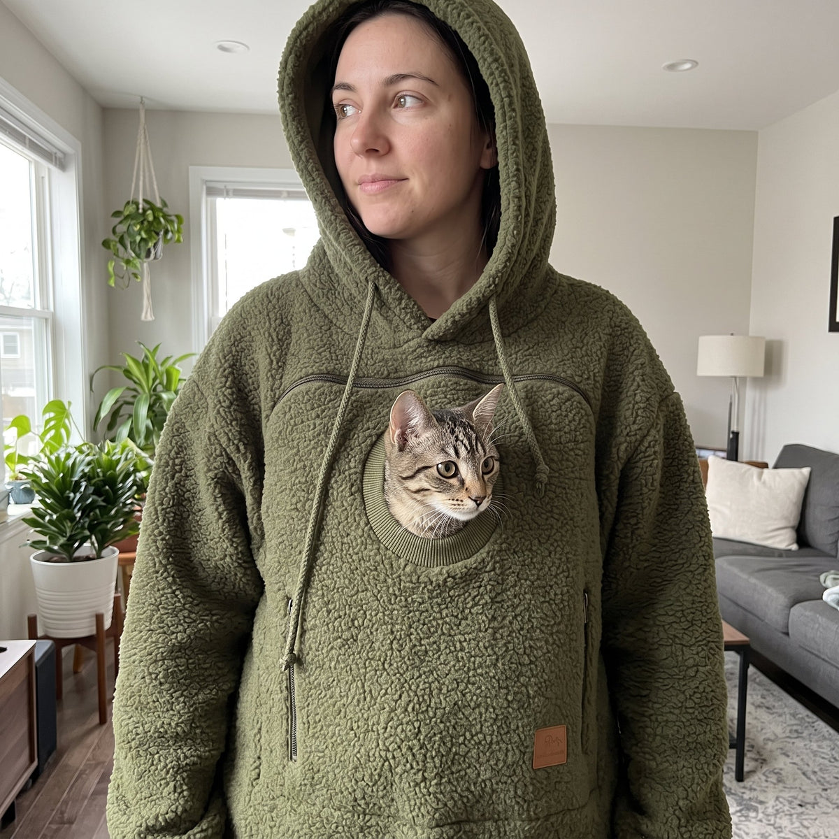 Tabby cat peeking out of the pouch of an army green Pawdie hoodie